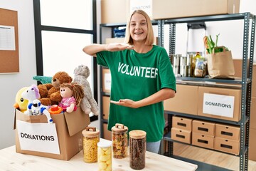 Young caucasian woman wearing volunteer t shirt at donations stand gesturing with hands showing big and large size sign, measure symbol. smiling looking at the camera. measuring concept.