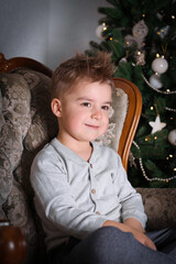 Little boy sitting by Christmas tree. Happy child, Christmas celebration.