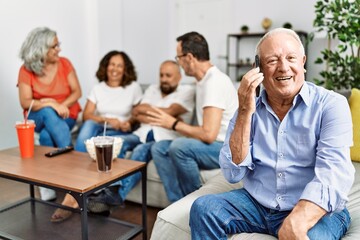 Group of middle age friends sitting on the sofa speaking. Man smiling happy talking on the smartphone at home.