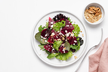 Beetroot salad with feta cheese and walnuts. Vegetable salad in plate on white background, top view