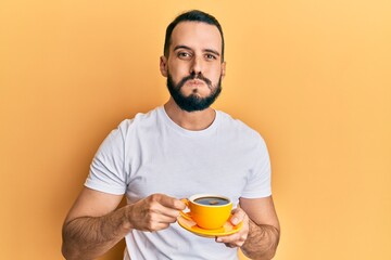 Young man with beard drinking a cup coffee puffing cheeks with funny face. mouth inflated with air,...