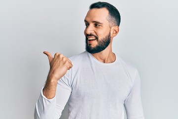 Fototapeta premium Young man with beard wearing casual white shirt pointing thumb up to the side smiling happy with open mouth