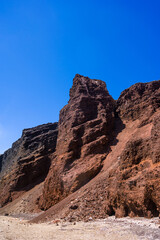 Huge red rock cliff on red sand beach Santorini. Alien landscape.