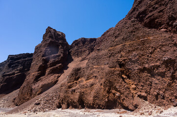 Huge red rock cliff on red sand beach Santorini. Alien landscape.