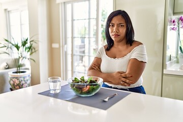 Obraz na płótnie Canvas Young hispanic woman eating healthy salad at home skeptic and nervous, disapproving expression on face with crossed arms. negative person.