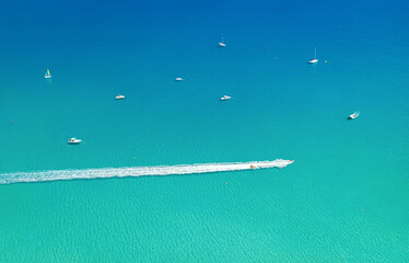 Speedboat and wave slider leaving trail on water, with other boats and sea as background with copy space. Aerial seascape