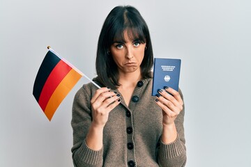 Naklejka premium Young hispanic woman holding germany flag and passport depressed and worry for distress, crying angry and afraid. sad expression.