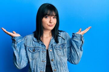 Young hispanic woman wearing casual denim jacket clueless and confused with open arms, no idea and doubtful face.