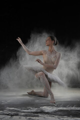 Obraz na płótnie Canvas beautiful ballerina dancing in white flour near a black wall