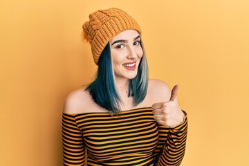 Young modern girl wearing wool hat doing happy thumbs up gesture with hand. approving expression looking at the camera showing success.