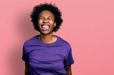 African american woman with afro hair wearing casual purple t shirt sticking tongue out happy with funny expression. emotion concept.
