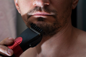 Process cutting beard handsome with trimmer. Young caucasian bearded man trimming beard in home...