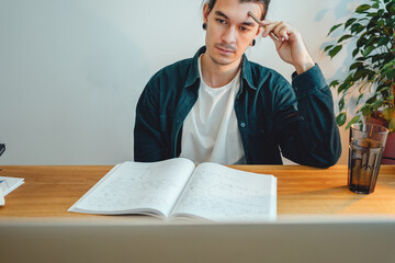 Pensive student making notes from laptop. Young man studying at home and prepare for pass exam