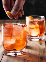 A man squeezes the zest of an orange over glasses with a Negroni cocktail. Vertical photo.