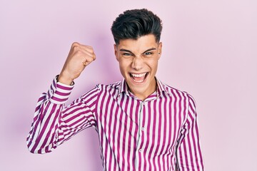 Young hispanic man wearing casual clothes angry and mad raising fist frustrated and furious while...