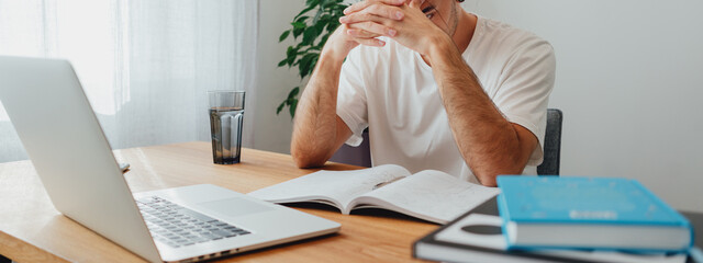 Pensive student making notes from laptop. Young man studying at home and prepare for pass exam....