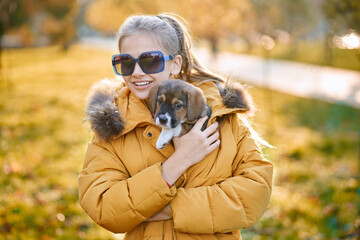 Close up of pretty girl in sunglasses hugging puppy in park. Conceot of walking with dog.