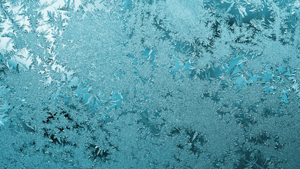 Light blue winter background or wallpaper. Drawing of ice crystals and frost on the window in...