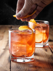 A man squeezes the zest of an orange over glasses with a Negroni cocktail. Vertical photo.