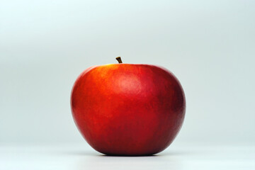 a fresh red apple isolated in graduated white background with back lighting and some dark shade of shadow