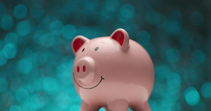 pink piggy bank rotating against blue background while bubbles are falling over it