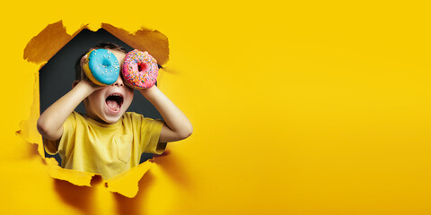 Happy cute boy is having fun played with donuts on Yellow background wall. Bright photo of a boy....