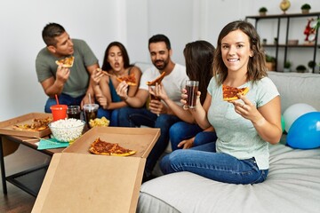 Group of young hispanic friends smiling happy eating italian pizza sitting on the sofa at home.