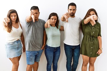 Group of young hispanic friends standing together over isolated background looking unhappy and...