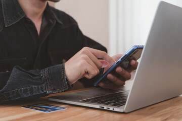 Online shopping using online payment. Hand typing smartphone with mock up credit card, laptop on wood desk in office. Quick and easy spending, Technology e-commerce, Online Market concept