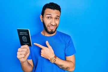 Hispanic man with beard holding italy passport pointing aside worried and nervous with forefinger,...