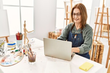 Middle age artist woman smiling happy using laptop at art studio.