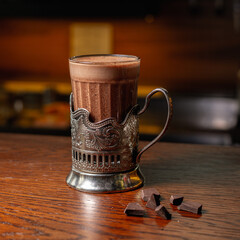 Glass cup in holder with hot cacao placed on wooden table in cozy cafe 
