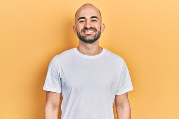 Young bald man wearing casual white t shirt with a happy and cool smile on face. lucky person.