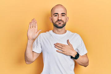 Young bald man wearing casual white t shirt swearing with hand on chest and open palm, making a loyalty promise oath