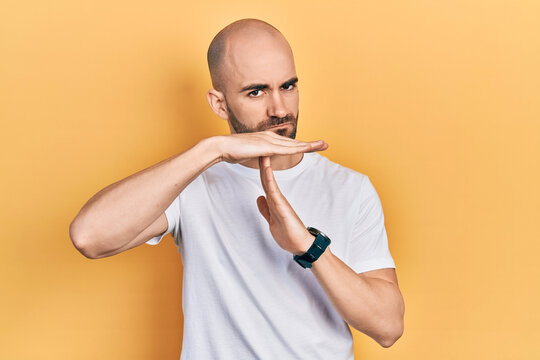 Young bald man wearing casual white t shirt doing time out gesture with hands, frustrated and serious face
