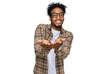 Young african american man with beard wearing casual clothes and glasses smiling with hands palms together receiving or giving gesture. hold and protection