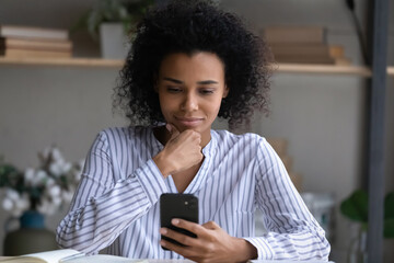 Young mixed race lady think on information on phone screen read professional news at corporate website chat with colleague at messenger. Focused black female office worker get business message by cell