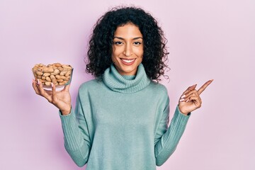 Young latin girl holding peanuts smiling happy pointing with hand and finger to the side