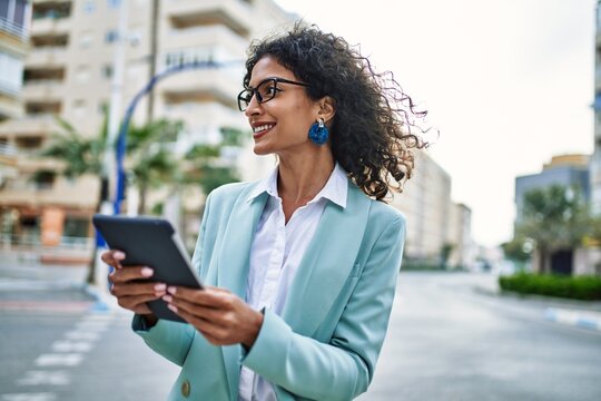 Young hispanic business woman wearing professional look smiling confident at the city using touchpad device