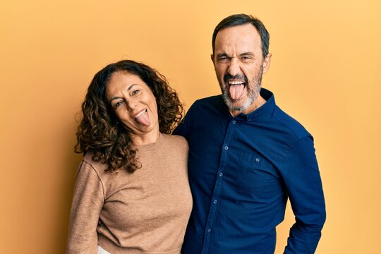 Middle age hispanic couple wearing casual clothes sticking tongue out happy with funny expression. emotion concept.