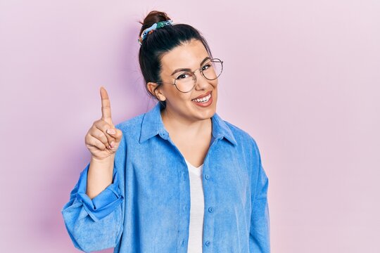 Young hispanic woman wearing casual clothes and glasses pointing finger up with successful idea. exited and happy. number one.