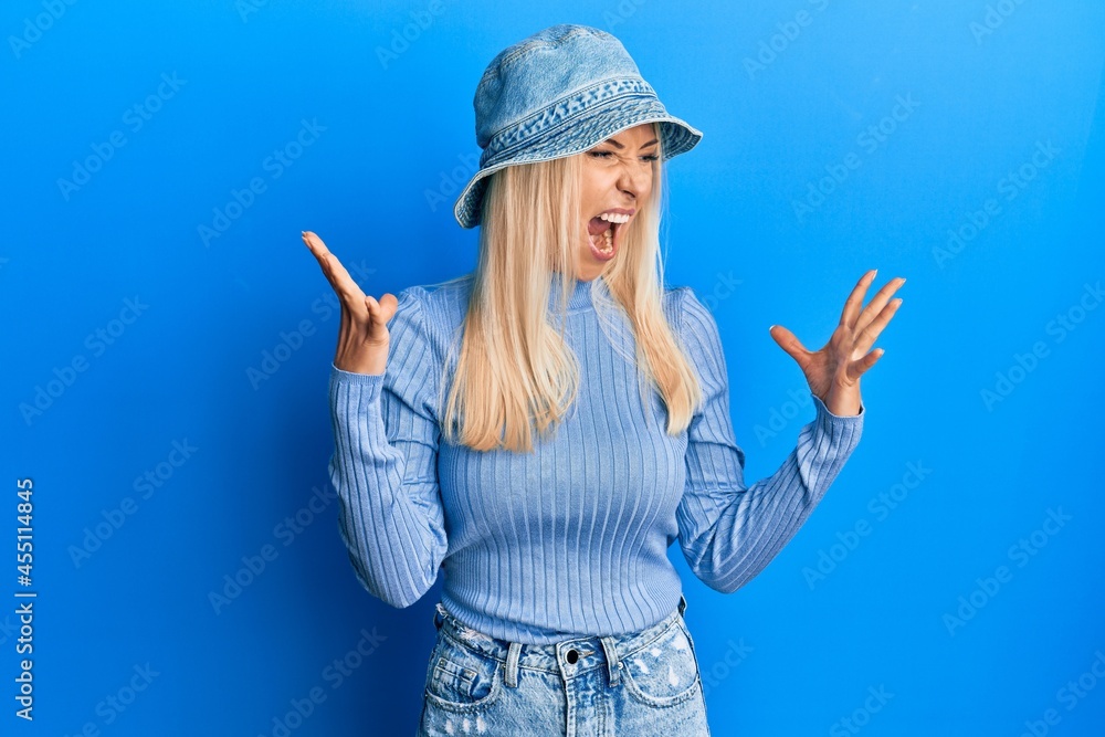 Poster young blonde woman wearing casual denim hat crazy and mad shouting and yelling with aggressive expre