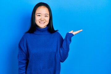 Young chinese girl wearing casual clothes smiling cheerful presenting and pointing with palm of hand looking at the camera.