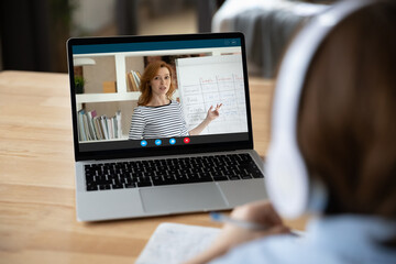Back rear view concentrated small kid boy in headphones holding educational video call meeting with teacher, learning foreign language remotely, studying on online courses, e-learning concept.