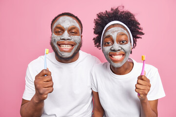 Happy ethnic woman and man apply clay masks on face to reduce fine lines and remove pores smile...