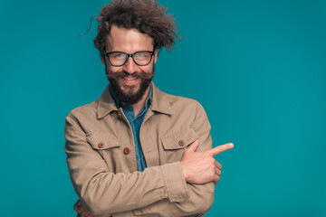 happy casual man in beige jacket with glasses pointing finger to side