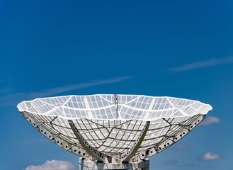 A giant satellite dish for receiving a signal is aimed up to the blue sky.
