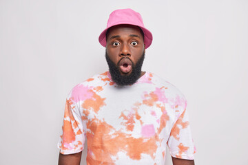 Shocked dark skinned Afro American man holds breath stares startled at something terrible wears...