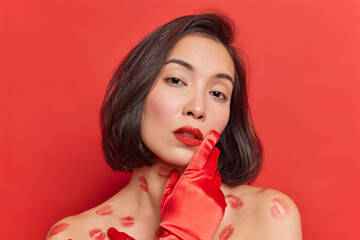 Portrait of gentle young Asian woman with clean healthy skin looks tenderly at camera has natural dark hair poses for magazine cover looks seductive isolated over vivid red studio background