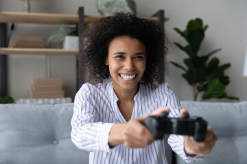 Enjoying videogame. Overjoyed african american gen z female sit on couch before tv screen holding...